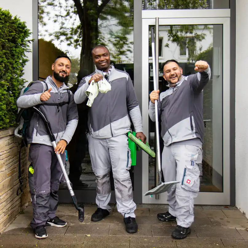 Drei gut gelaunte Mitarbeiter des raumgut Facility Teams stehen zusammen vor einem Hauseingang und lachen in die Kamera.