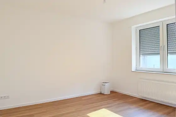 Frisch renovierter Raum in Mietwohnung, mit Fenster, weiße Wände und neuer Laminatboden in hellem Braun