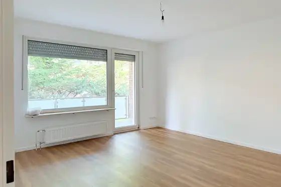 Wohnzimmer mit Balkonzugang nach der Renovierung. Frische weiße Wände und neuer Laminatboden