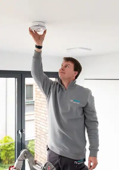 Ein Mitarbeiter befestigt einen Rauchwarnmelder unter der Decke